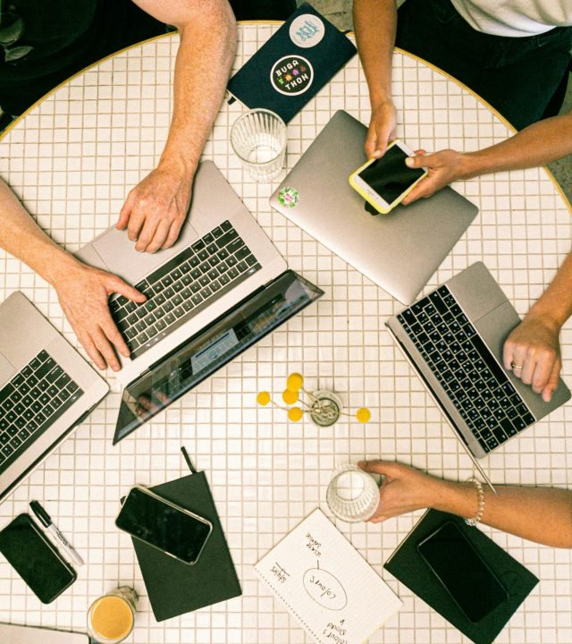 Top view of a team collaborating with laptops, phones, and notes in a modern office.